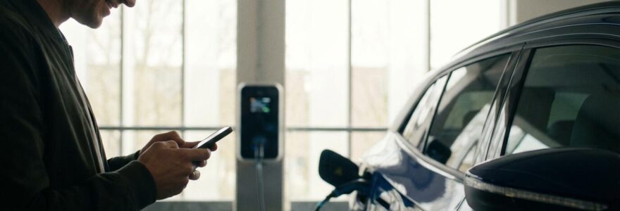 Conducteur vérifiant son kilométrage LLD électrique sur smartphone près d'une borne de recharge